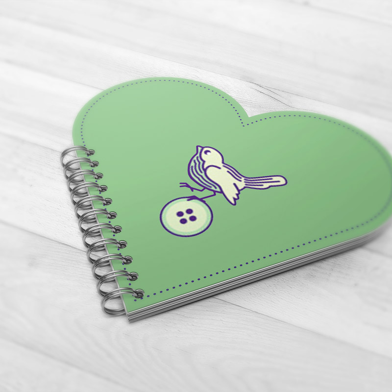 mint green heart shaped notebook featuring a bird sitting on a button logo