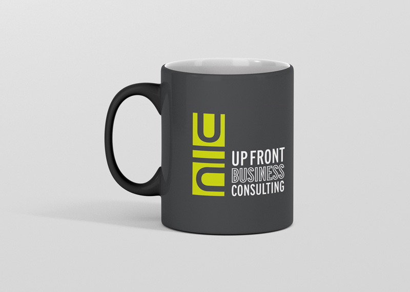 Dark grey coffee mug featuring a stacked green block logo for Up Front Business Consulting